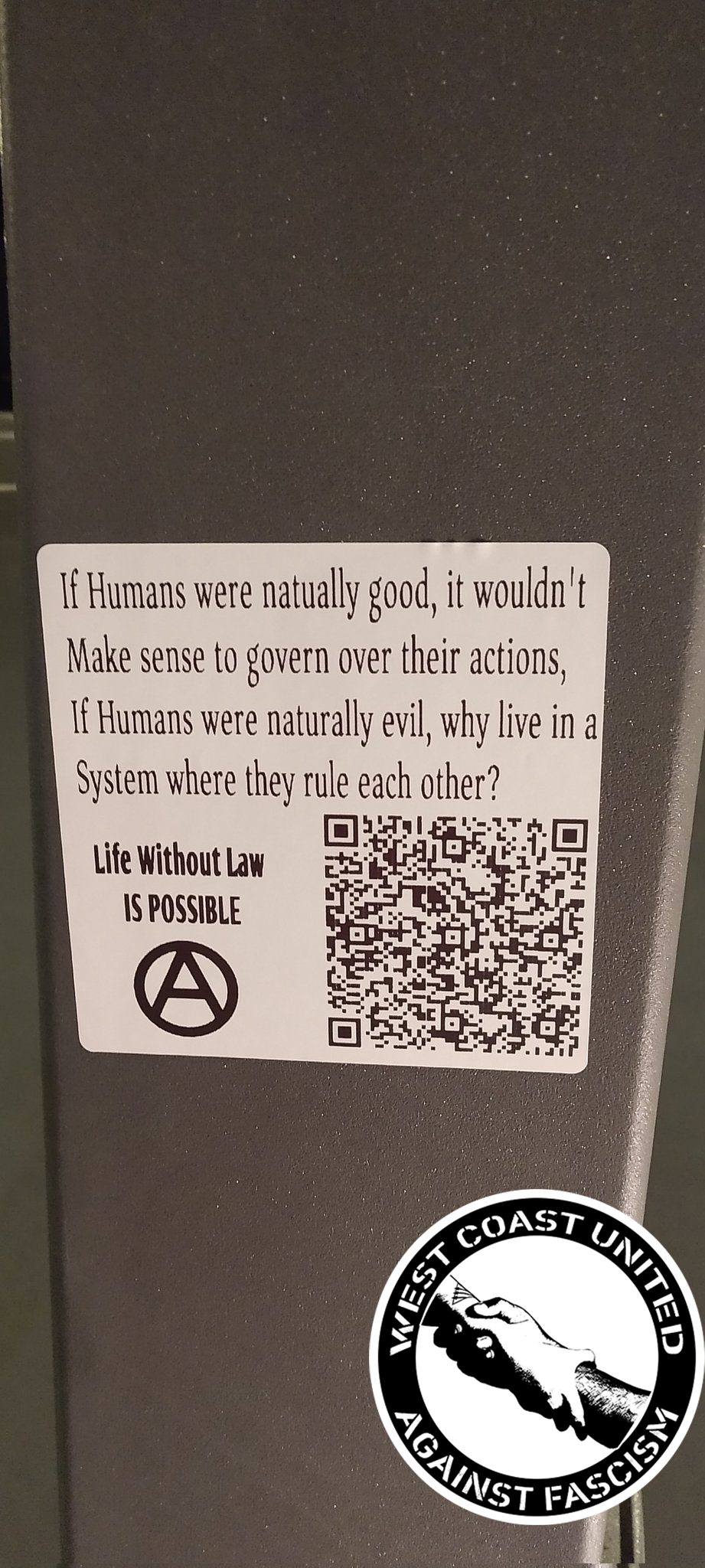 A square sticker on a variousu object reads "If Humans were naturally good, it wouldn't Make sense to govern over their actions, if Humans were naturally evil, why live in a system where they rule each other? Life without Law is possible." It includes an anarchist "circle a" and a QR code.