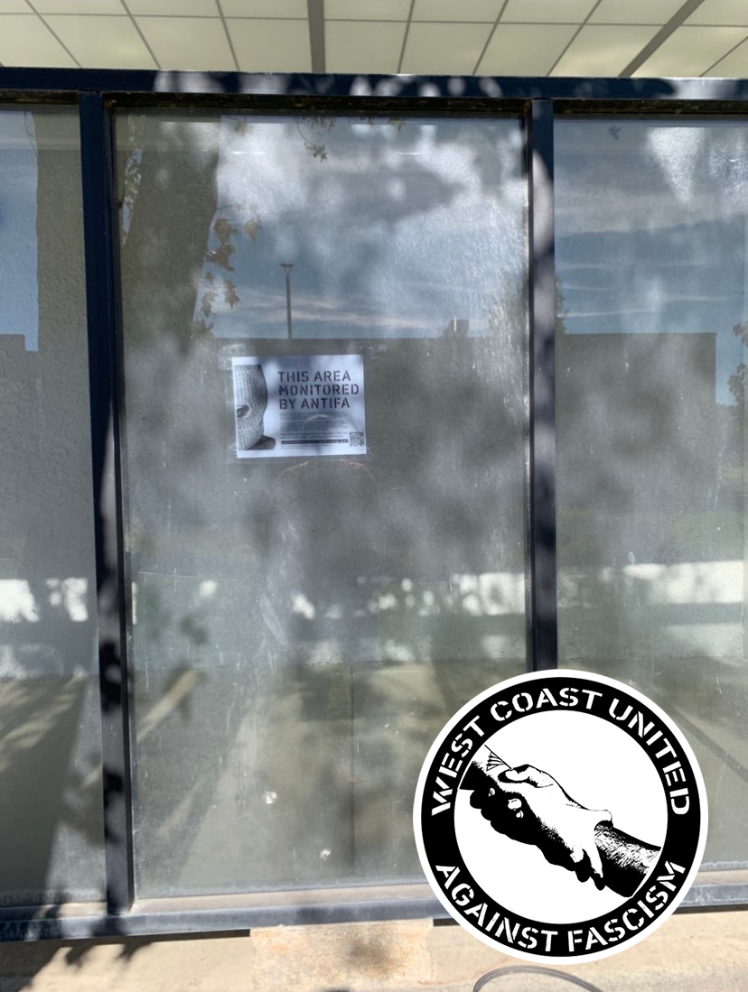 What appears to be a shelter for a bus stop has a flyer adheared to it. On the left side it has a ski mask thats cut in half, staring ominously. The top right reads "This area monitored by Antifa."